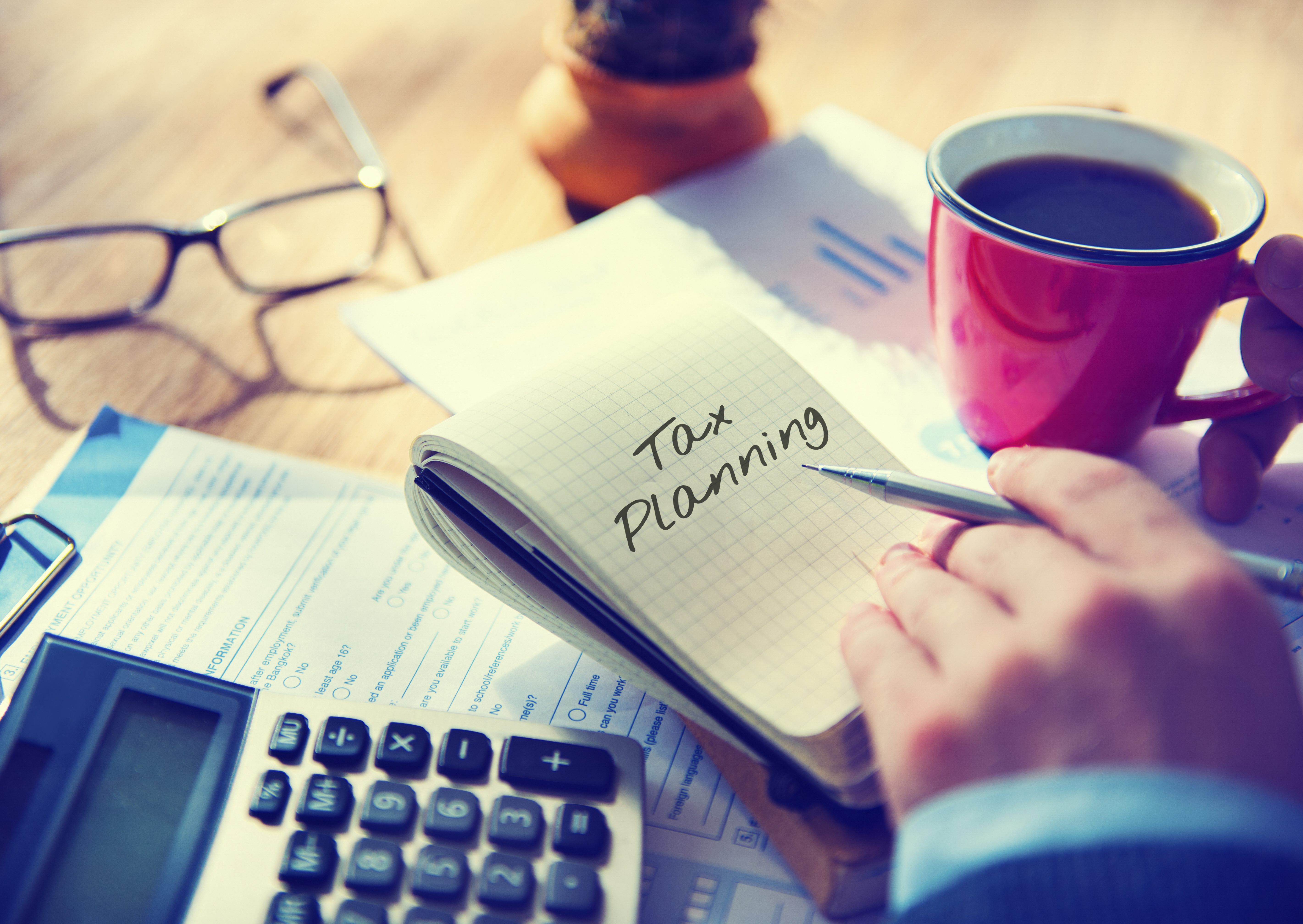 Desk with calculator, coffee, and notepad with the words "tax planning"