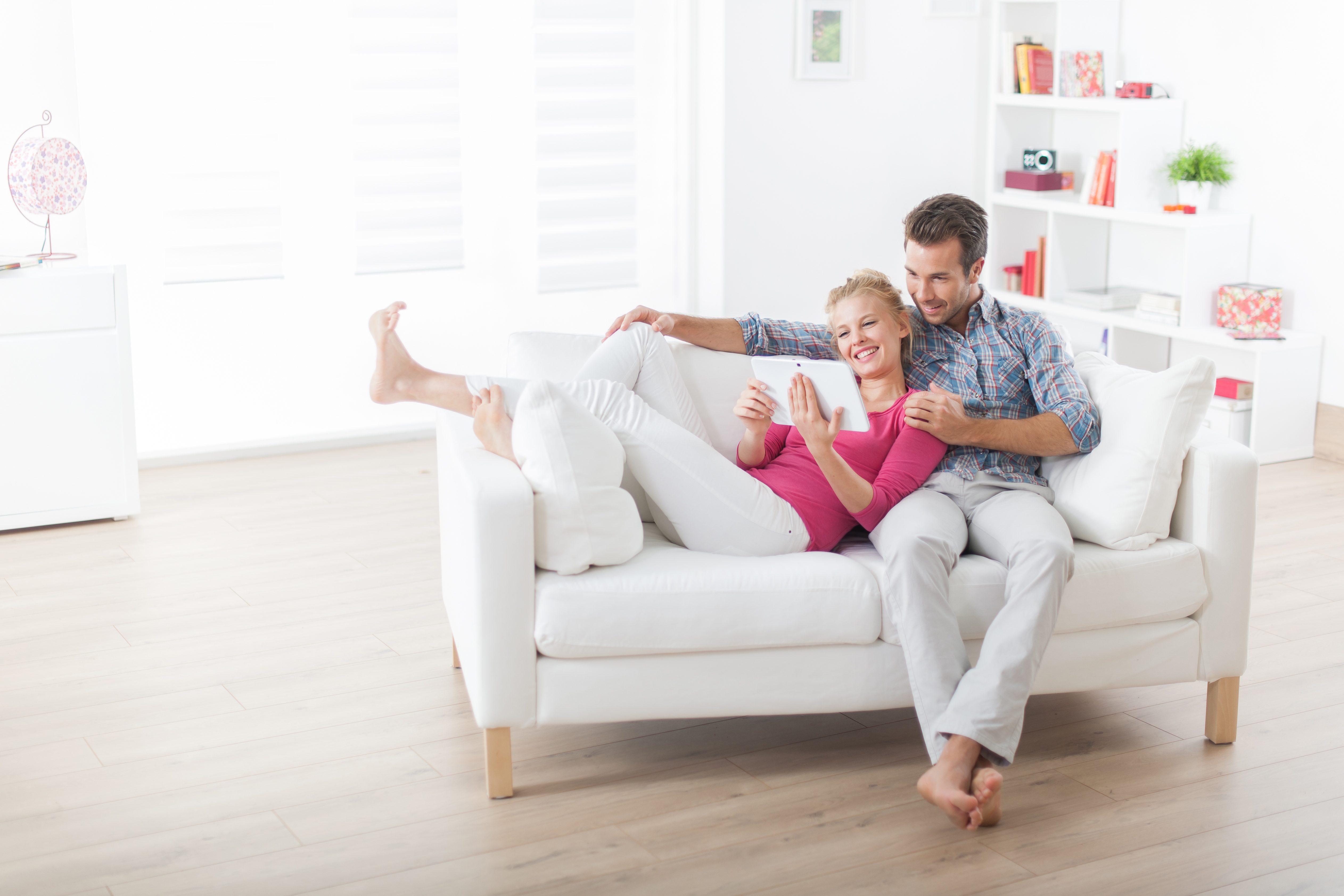 Millennial couple lounging on a modern sofa looking at a Tablet